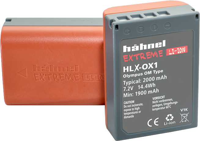 Kuvassa on kaksi harmaata ja oranssia Hähnel Battery Extreme Olympus HLX-OX1 / BLX-1 -akkuakkua: toinen on pystyssä ja näyttää etikettinsä ja tekniset tiedot, kun taas toinen makaa litteänä taustalla.