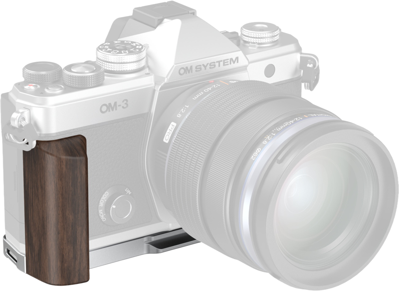 The picture shows a digital camera marked "OM System OM-3" with a SmallRig 5563 L-shaped mounting plate and wooden handle attached to the left side for improved ergonomics and functionality.