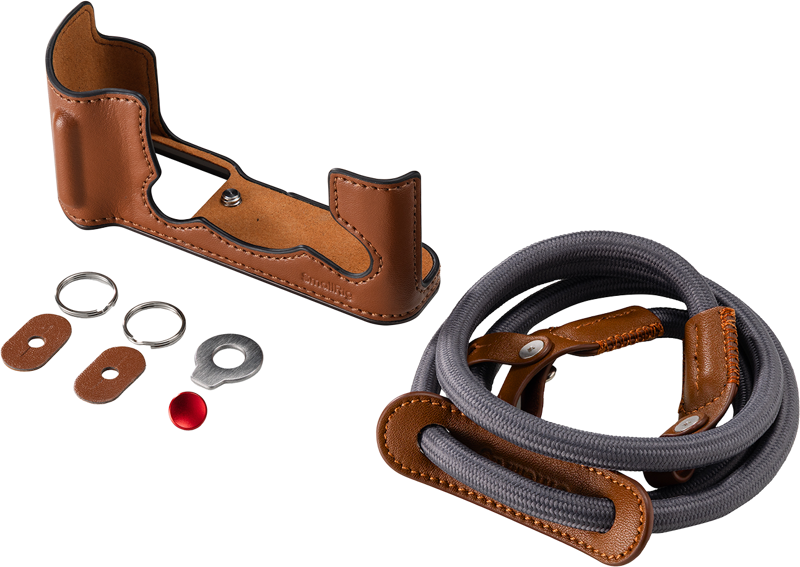 SmallRig 5670 Leather Half Case Kit for Fujifilm X-T30/II/III (ruskea) sisältää ruskean nahkaisen puolikotelon, yhteensopivan hihnan nahkakoristeilla, kaksi metallirengasta, kaksi nahkaista rengassuojaa, metallisen aluslevyn ja pienen punaisen painikkeen vaalealla pohjalla.
